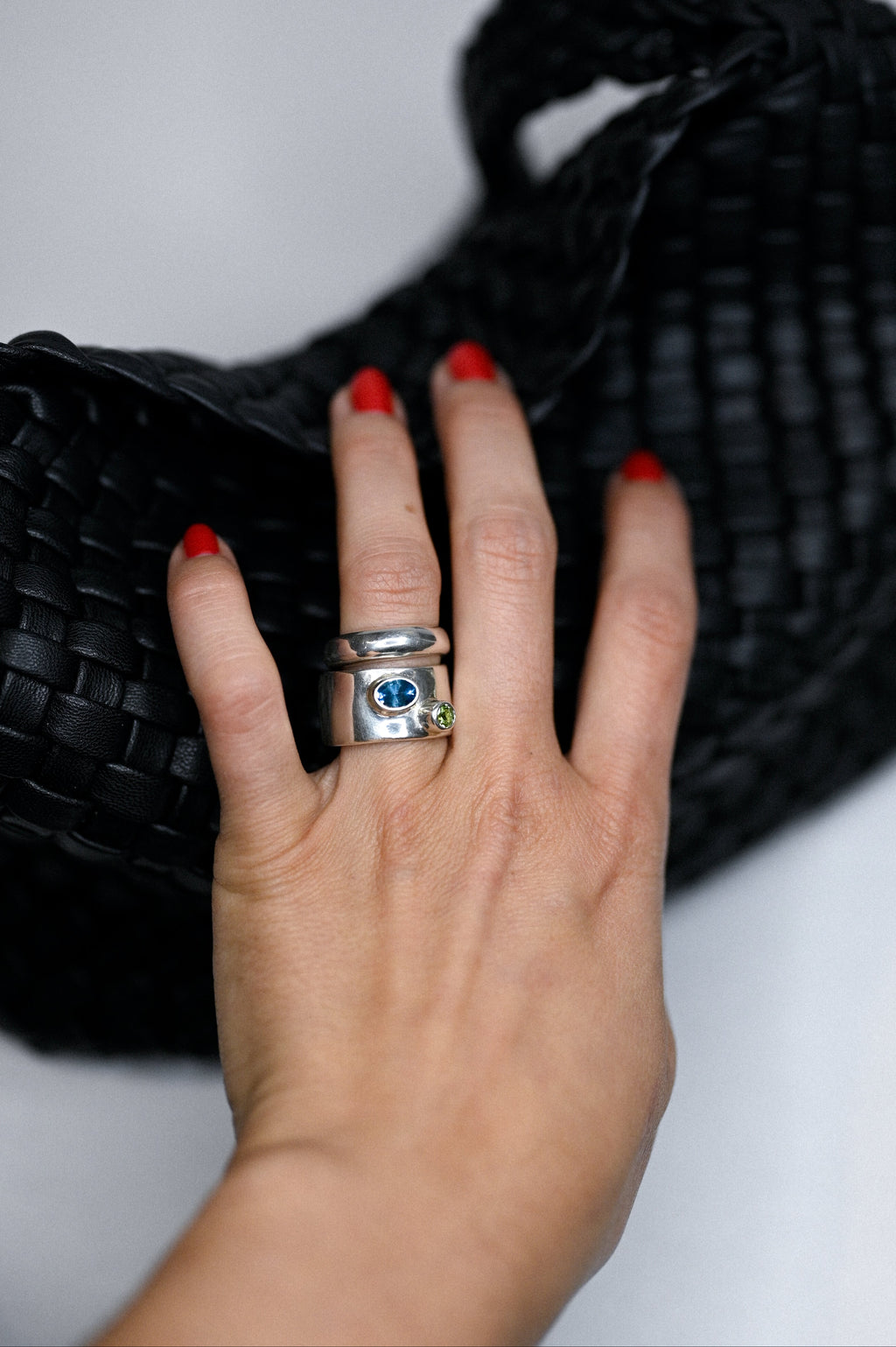 Hand holding a silver ring with gemstones on a white background