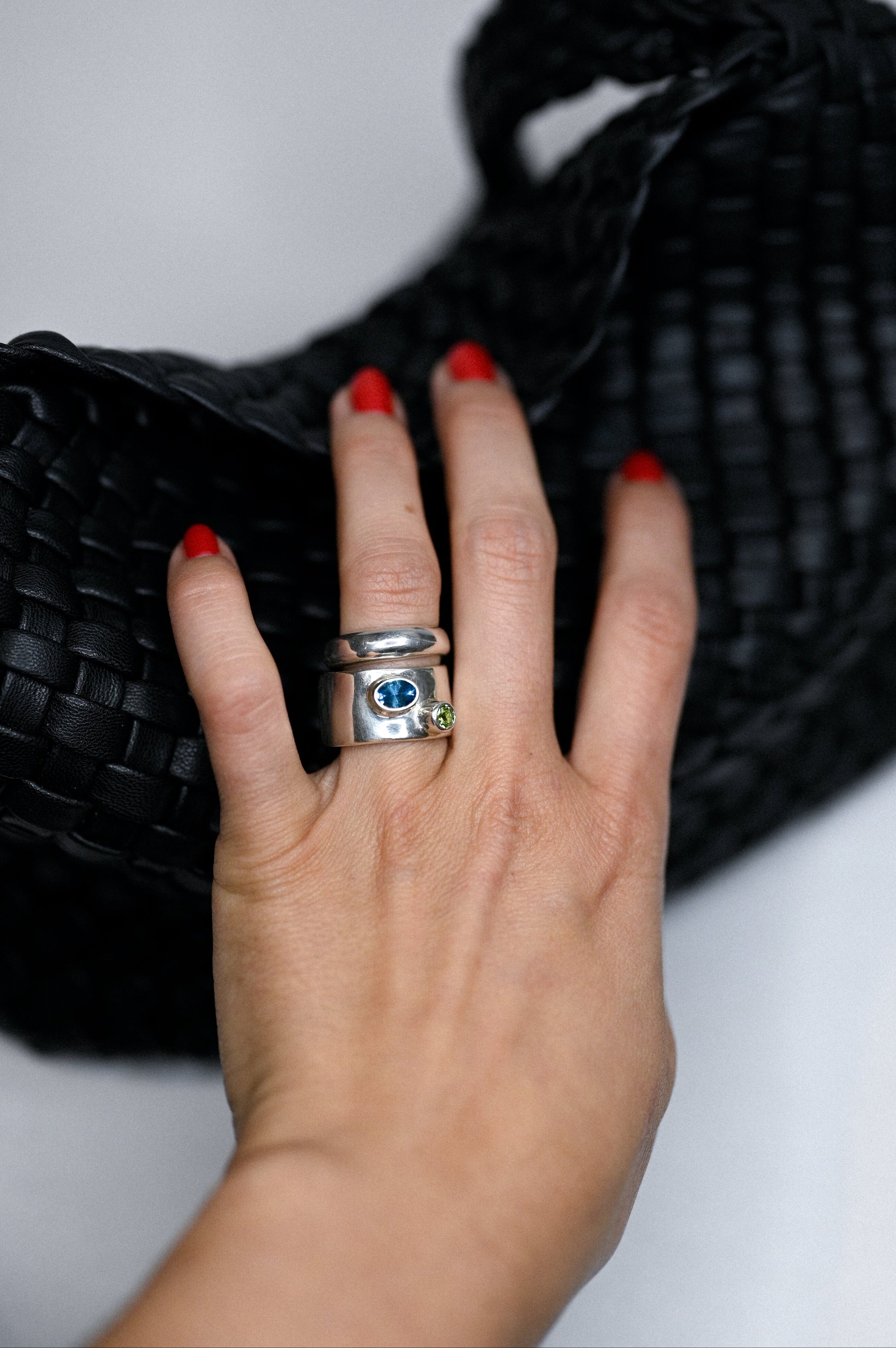 Hand holding a silver ring with gemstones on a white background